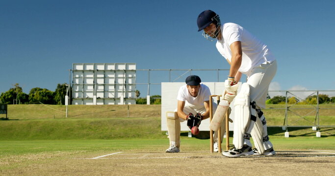 Batting batsman holding bat wearing helmet facing crouching keeper on cricket pitch, copy space - Powered by Adobe