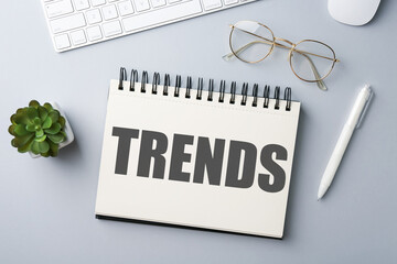 Trends inscription in notebook, computer keyboard, glasses and pen on white table, top view