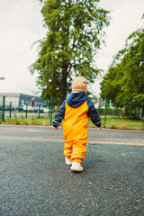 Fototapeta premium A cheerful child in bright orange rain gear walks joyfully along a wet road, surrounded by lush green trees, creating a delightful moment in nature and embracing the wonders of childhood