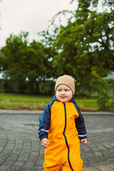A joyful child in colorful rain gear plays outdoors, embracing nature despite dark clouds. This...
