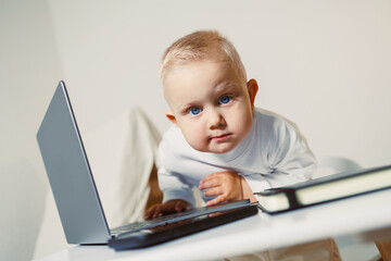 An adorable and curious baby is intently exploring a laptop while sitting on a stylish desk in a...