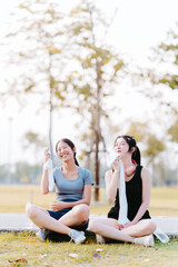 Two Asian girls sit and relax while exercising in the park, health care concept