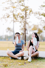 Two Asian girls sit and relax while exercising in the park, health care concept