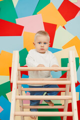 A cute and lively toddler enthusiastically climbs a sturdy wooden ladder within a vibrant,...