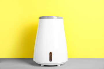 Modern humidifier on table near yellow wall