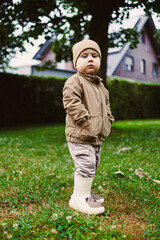 A charming boy in casual outdoor attire stands joyfully in a lush green field, showing a playful...