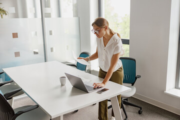 A focused and determined woman collaborates intensely at a sleek office desk with her laptop and...