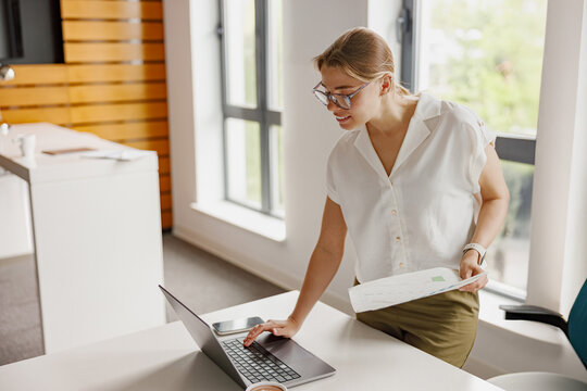 A focused woman diligently analyzing complex data on her laptop inside a contemporary office environment - Powered by Adobe