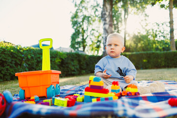 A joyful toddler plays on a cozy blanket in the grass, surrounded by colorful toys under a sunny...