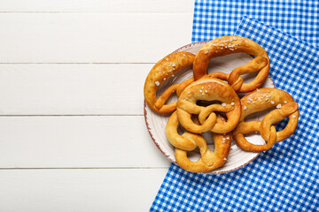 Plate with soft pretzels and napkin on white wooden background