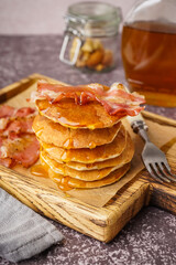 Wooden board of tasty pancakes with bacon and maple syrup on table