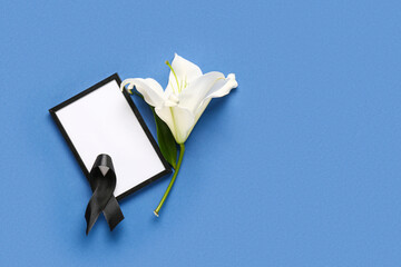 Black ribbon with photo frame and white lily flower on blue background