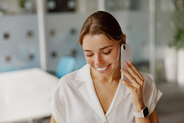 A cheerful and smiling woman is engaged in a phone conversation in a stylish and modern office...