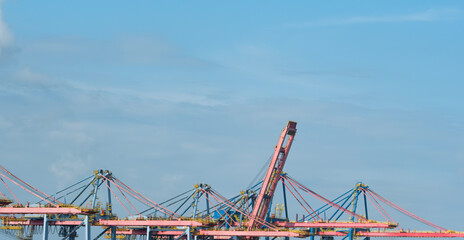 Colorful port cranes with raised boom at a shipping terminal under a bright blue sky, ready for container loading and unloading