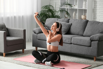Beautiful young woman training with fitness expander on yoga mat in living room