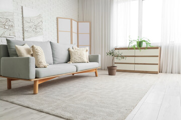 Interior of stylish living room with comfortable sofa, folding screen, chest of drawers and carpet