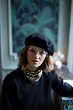 Headshot of young beautiful woman with glasses and berett looking strait into lance.