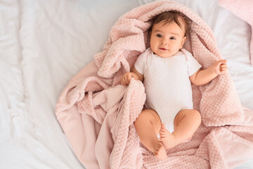 Cute little baby with pink plaid lying on bed, top view