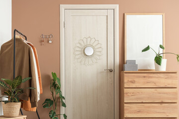Interior of stylish hall with clothes rack, door, chest of drawers and key holder on beige wall