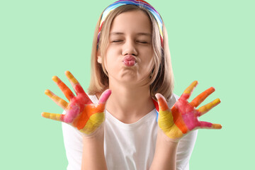Smiling teenage girl with painted hands blowing kiss on turquoise background