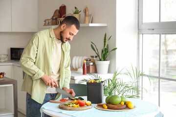 Young man with compost bin and vegetable scraps during cooking in kitchen