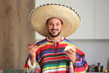Young Mexican man with tasty taco and chilli in kitchen