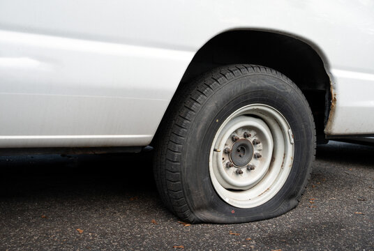 Close-up and detailed image of a flat car tire, showing visible deflation and rubber damage.