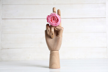 Mannequin hand with pink rose on white wooden table