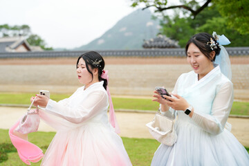 In Seoul in June 2025, two Korean women in their twenties wear pink and sky-blue hanbok as they...