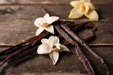 Fototapeta premium Dried vanilla sticks and flowers on wooden background, closeup