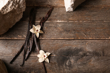 Dried vanilla sticks with flowers and stones on wooden background