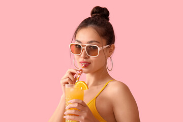 Pretty young woman in swimsuit with glass of orange juice and straw on pink background