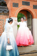 In Seoul in June 2025, two Korean women in their twenties wearing pink and sky-blue hanbok stand in...