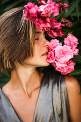 Naklejka premium Head shot of fashion model smelling on beautiful pink flower. Natural beautiful woman with no make up with blossoms, cosmetics concept, natural beauty, skin care