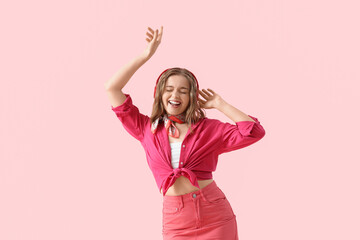 Cool young woman listening to music and dancing on pink background