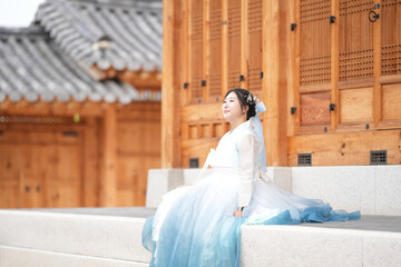 A Korean woman in her twenties wearing a sky-blue hanbok sits in front of the Gyeongbokgung Palace...