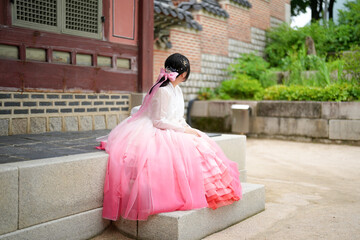 A Korean woman in her twenties wearing a charming pink hanbok sits in front of the traditional...