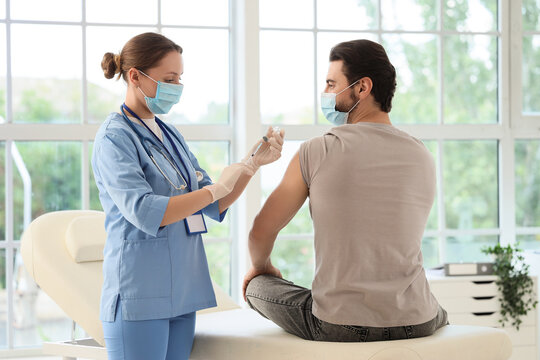Young man with medical mask receiving vaccine from doctor in clinic