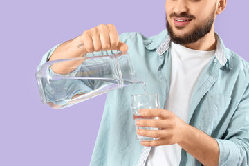 Young man pouring water into glass on lilac background, closeup