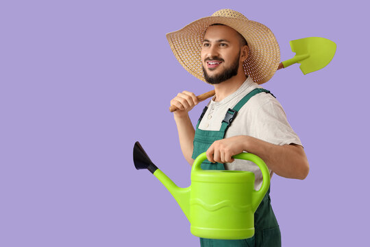 Male gardener with watering can and shovel on lilac background