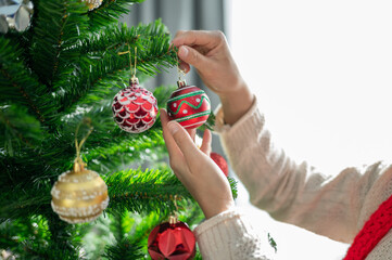 Cropped shot view of woman hands decorating Christmas tree during Christmas festival and New Year celebration.