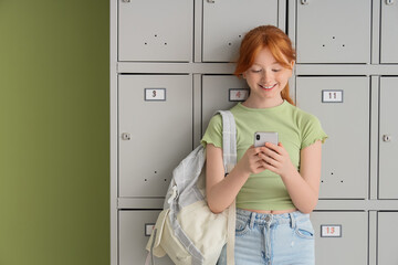 Teenage schoolgirl using mobile phone near locker on green background