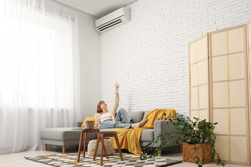 Young woman lying on sofa with air conditioner at home