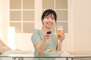 夕食に晩酌しながらテレビを見ながら笑う若いアジア人女性
