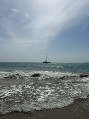 Sailboat sailing on calm sea with waves crashing on shore