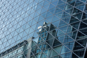 A grid of triangular glass panels creates a modern facade, reflecting nearby buildings. Contemporary designed mirrored surfaces capture urban architecture with geometric precision.