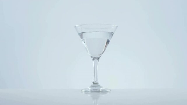 Gold confetti swirling revealing glass, olive skewer dropping causing splash, celebrating cocktail