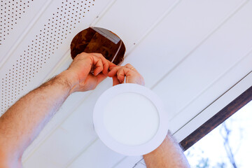 Electrical carefully secure new light fixture into ceiling while renovating indoors on work day.