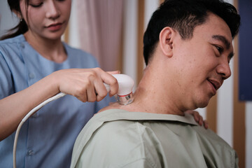 Closeup shot, male Asian patient is recovery treated, gel ultrasound shoulder pain relief by female...