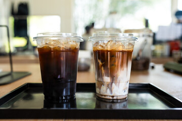 Two glass of iced latte and iced americano in cafe served on black tray